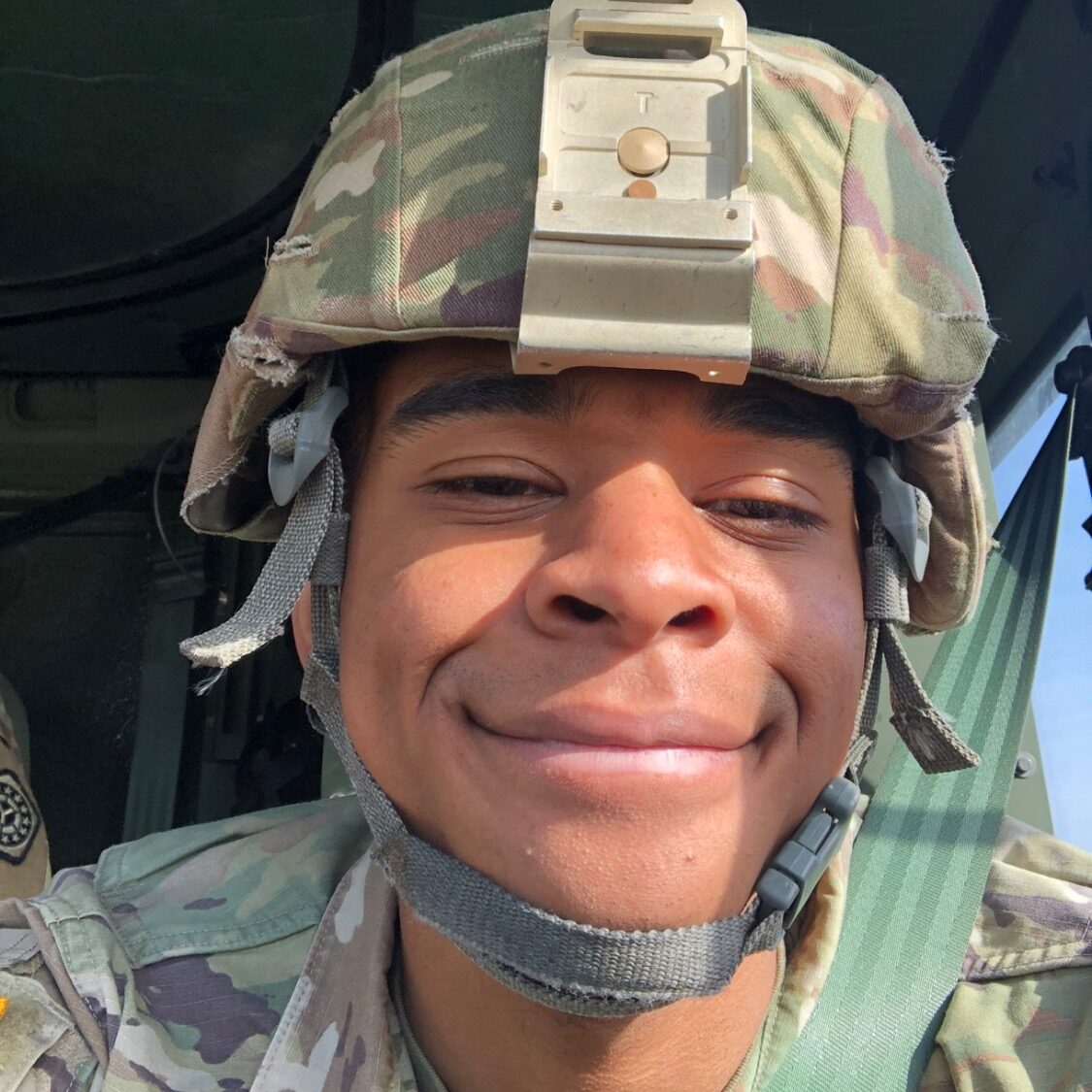 Service member smiles for a picture.  Soldier wears an army uniform and army helmet. 